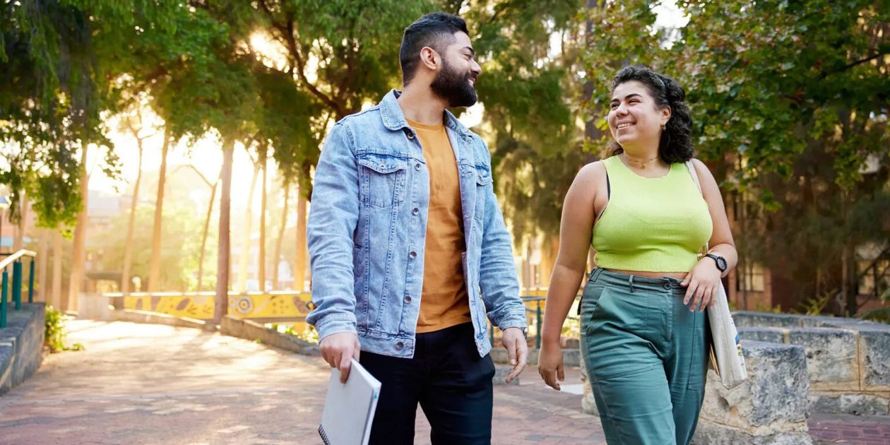 Two Curtin University students smiling at each other while walking to the right