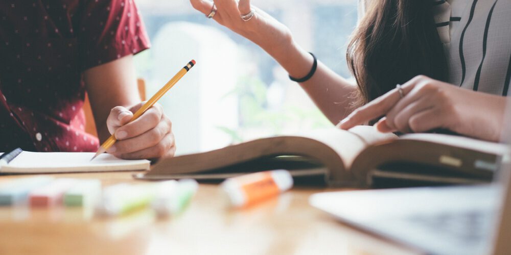 Two high school students studying with a book and notepad.