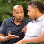 Father and son sitting on a garden bench. Father is giving his son some advice.