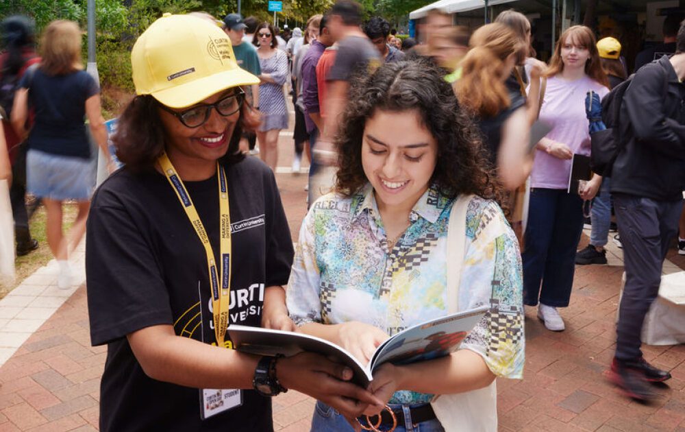 Female student receiving advice from a helper at Curtin Open Day, and looking through a Curtin course guide.