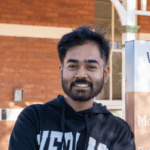 Aquib stands smiling in front of WA School Of Mines in Kalgoorlie