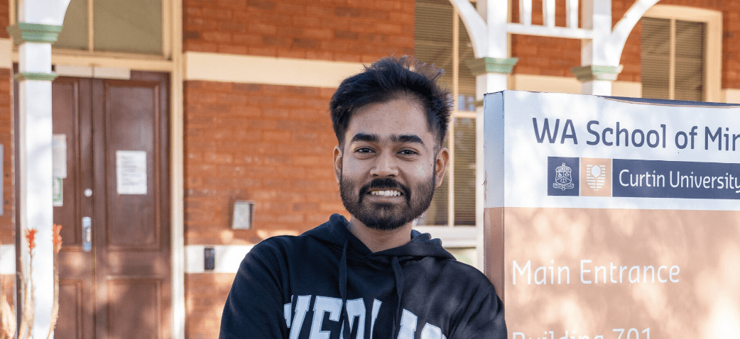 Aquib stands smiling in front of WA School Of Mines in Kalgoorlie