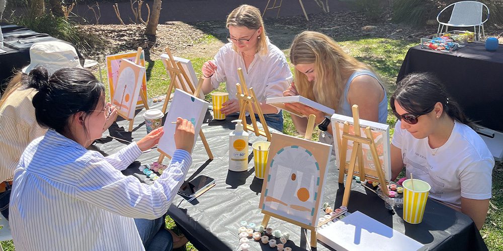A group of students outdoors painting on a table.