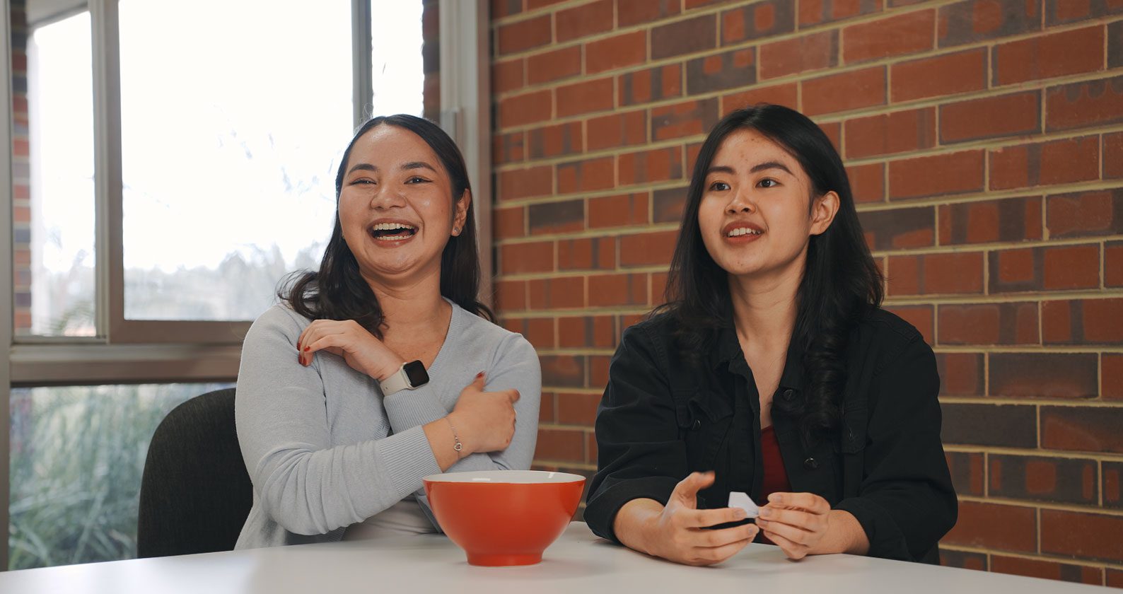 Celena and Devna sit at a table selecting questions out of a bowl.