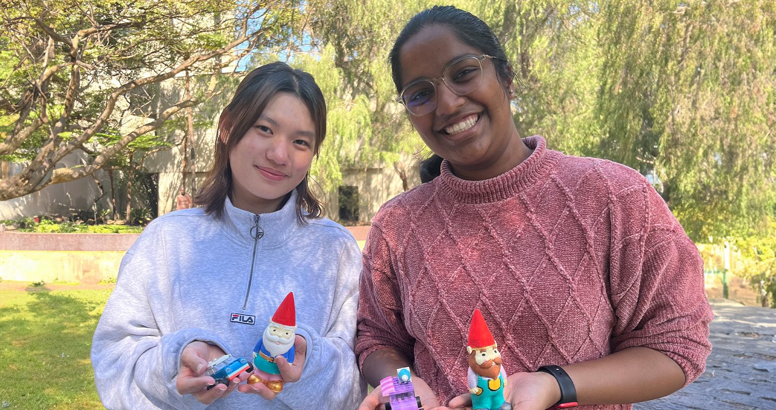 Two students stand outdoors holding painted gnomes.