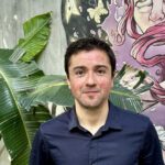 Pablo, a Master of Environment and Climate Emergency student smiles in front of a campus mural.