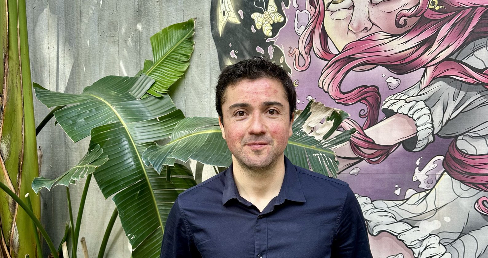 Pablo, a Master of Environment and Climate Emergency student smiles in front of a campus mural.