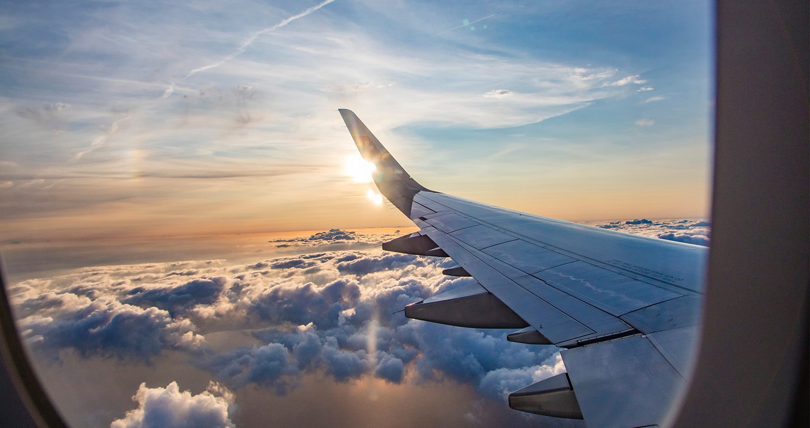 A view from inside a plane out a window looking at the sky and a plane wing.