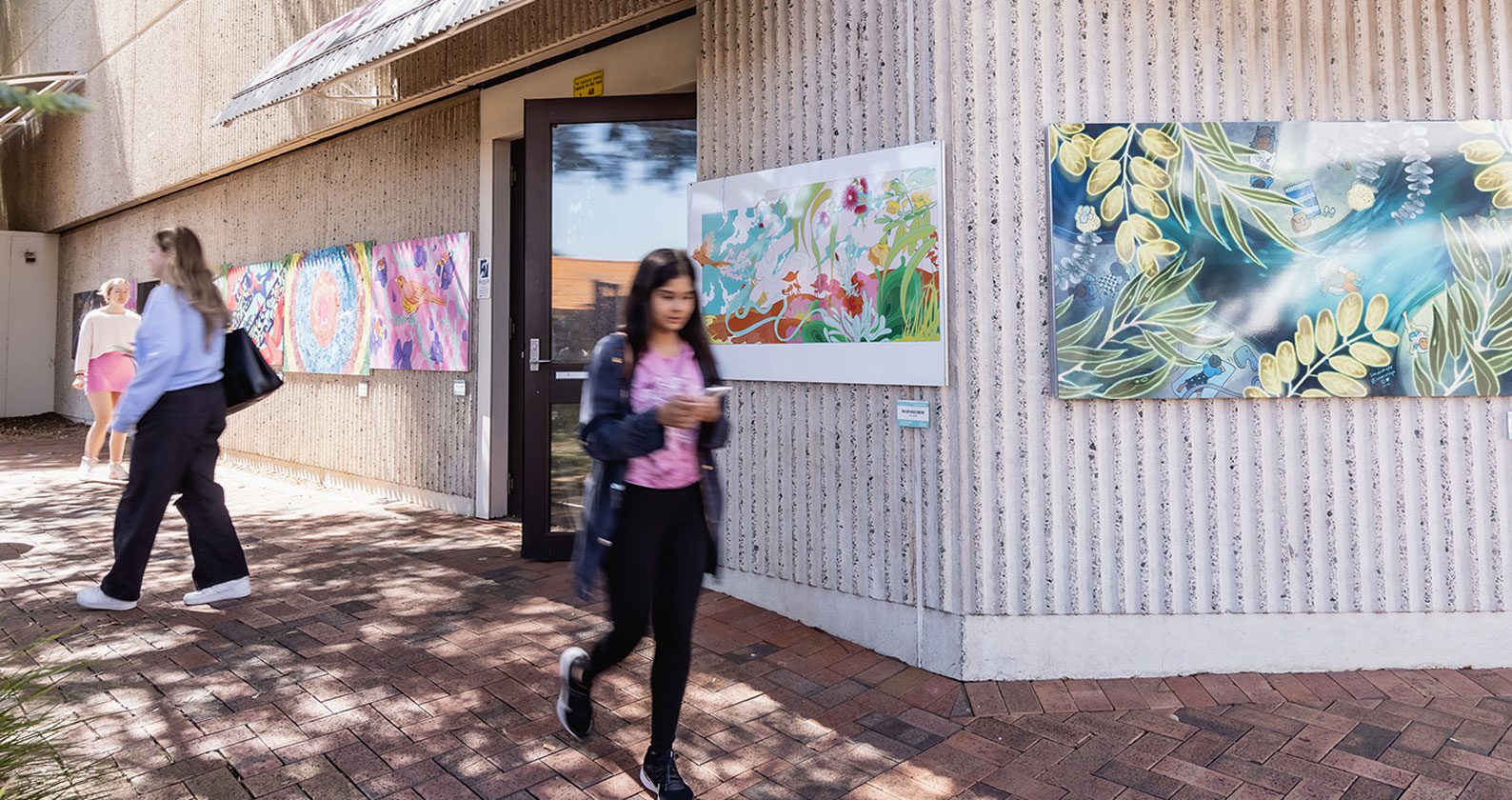Students walking outside a building with art on the walls.