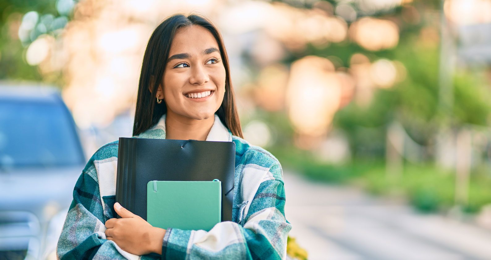 A student holding books and smiling into the distance.