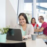 Woman with a laptop open in front of her, sitting in a cafe