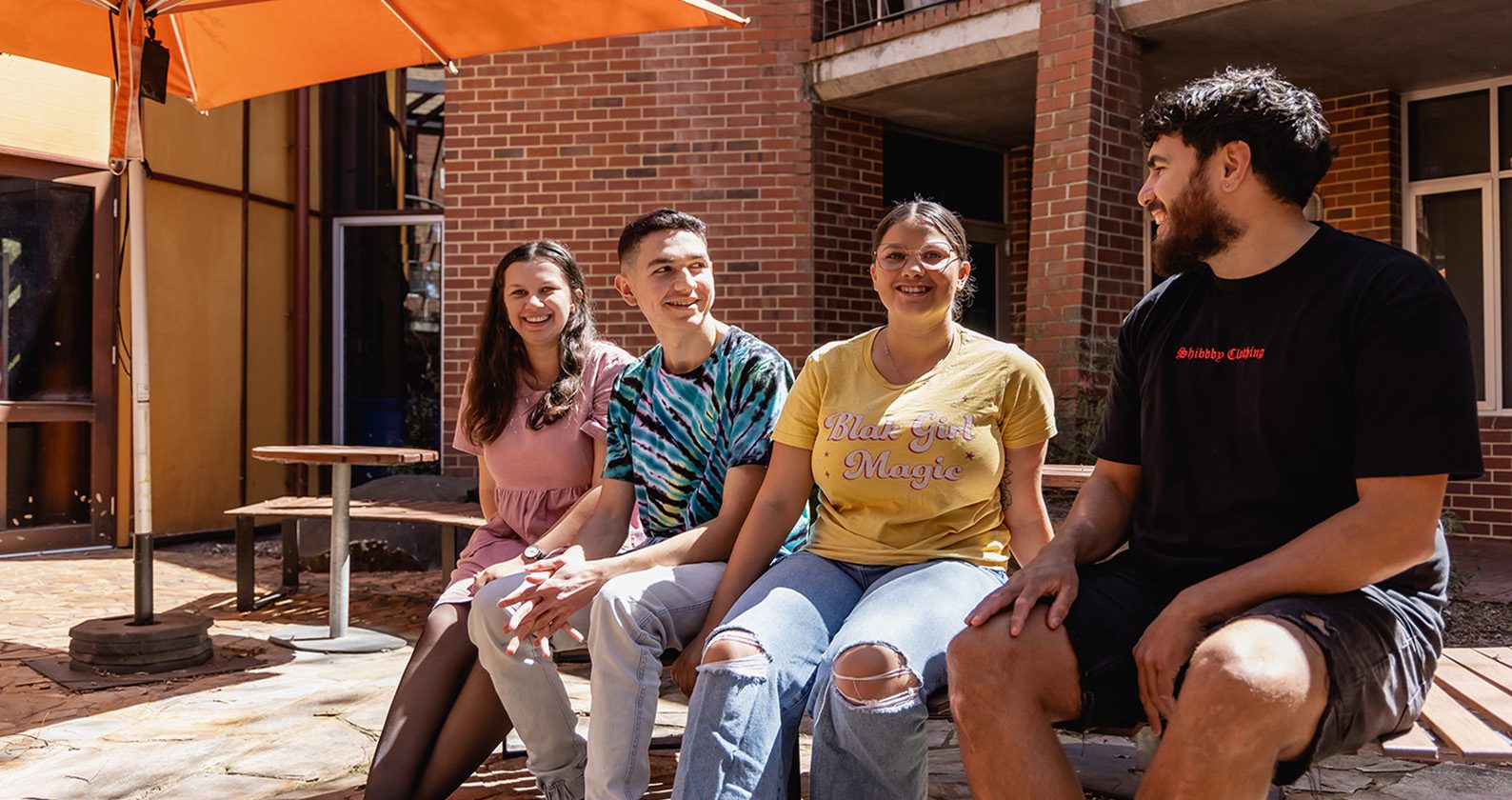 Four students sit together on a bench out the front of the Centre of Aboriginal Studies.