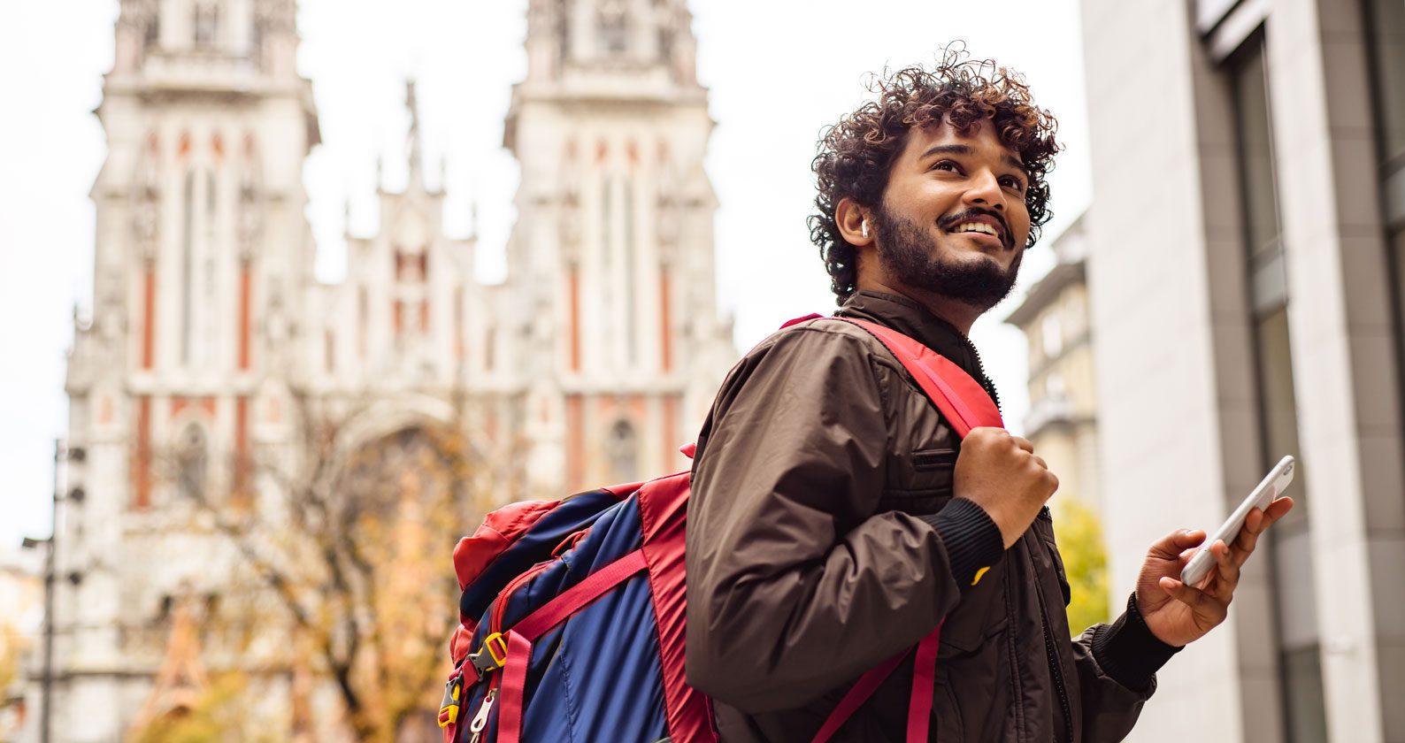 Man smiling with a backpack on. He is standing in front of an old building,