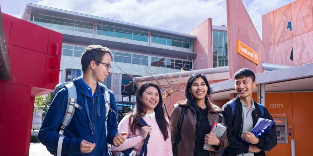 Four Curtin University students walking through the Curtin Bentley campus and smiling.