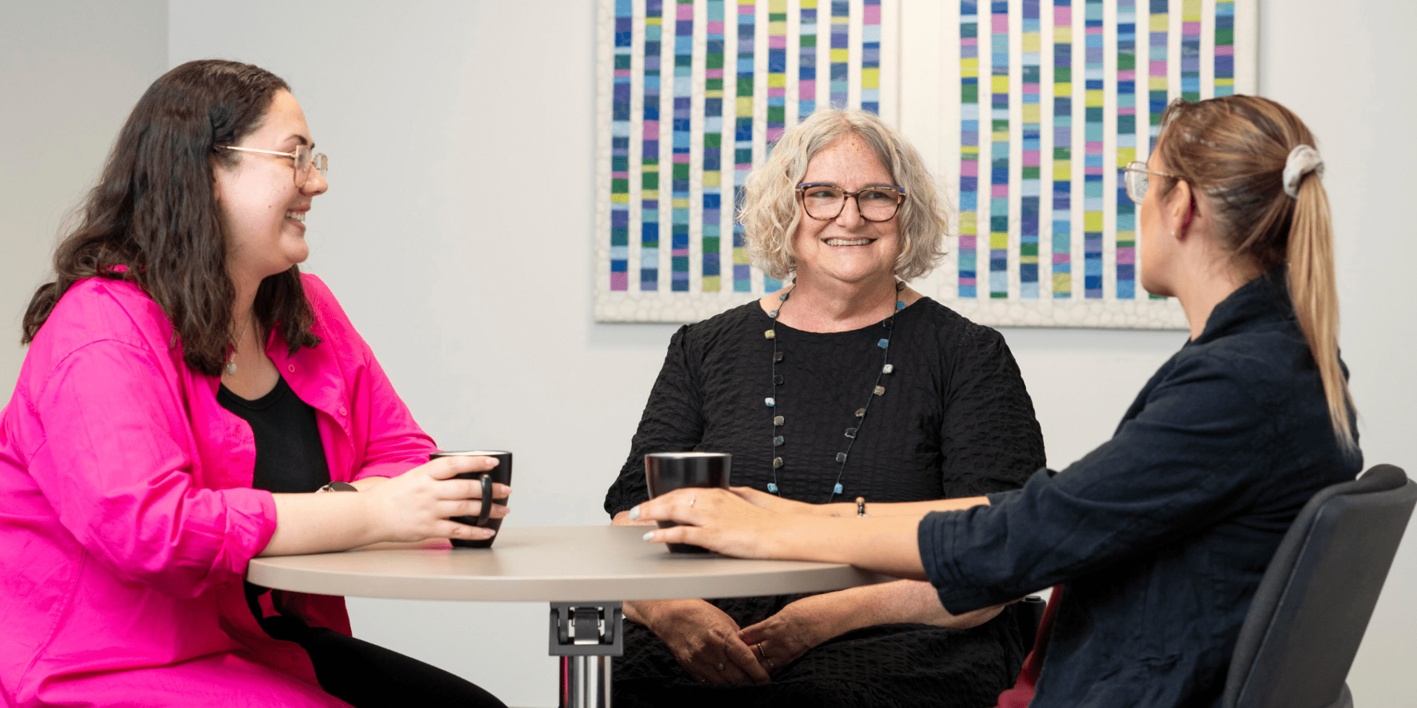 Three women sitting at a desk in an office setting. Image depicts micro-level and mezzo-level social work.