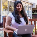 Person sitting on a bench on a laptop.
