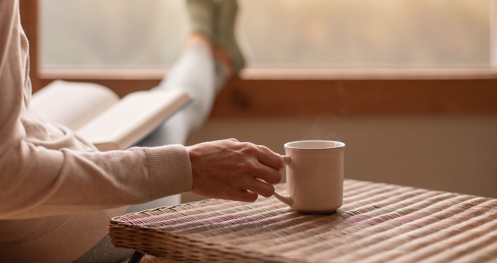 A person holds a cup of tea while reading a book and relaxing.