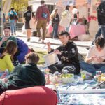 Multiple students sitting on a picnic blanket playing with crafts.