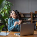 A woman looking off into the distance while sitting at a table with a laptop.