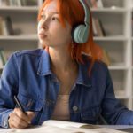 Student looking off into the distance wearing headphones while sitting at a desk with a laptop.