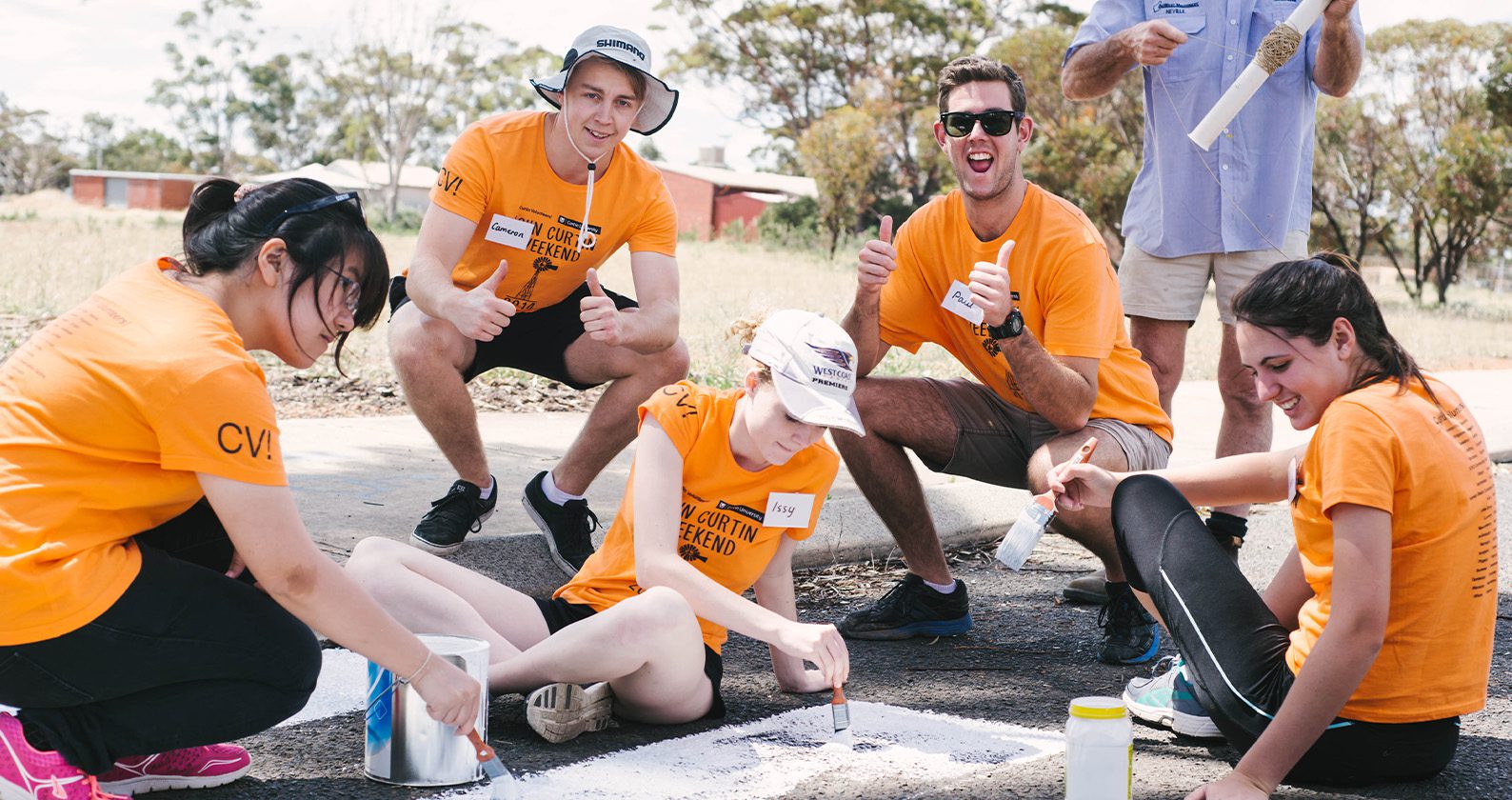 Four students helping paint white lines on a road.
