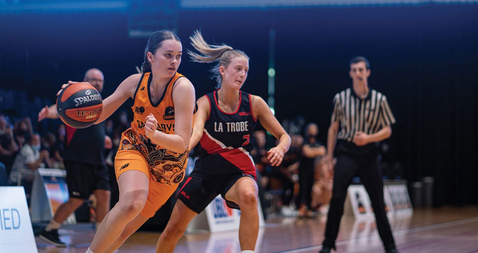 Two students playing basketball run across the court.