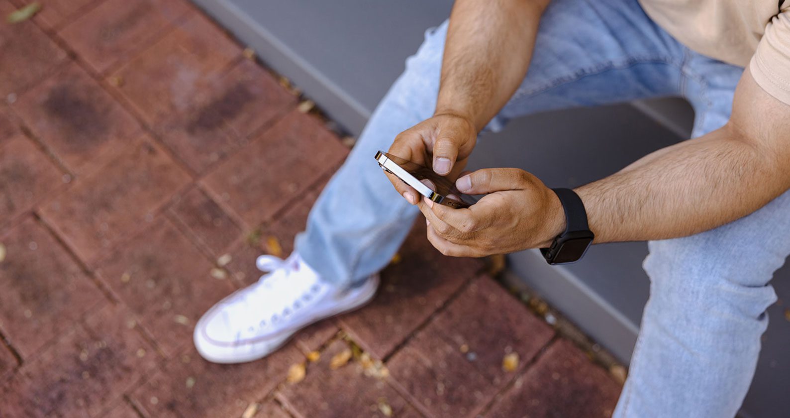 Student sitting on a step with a phone in their hands.