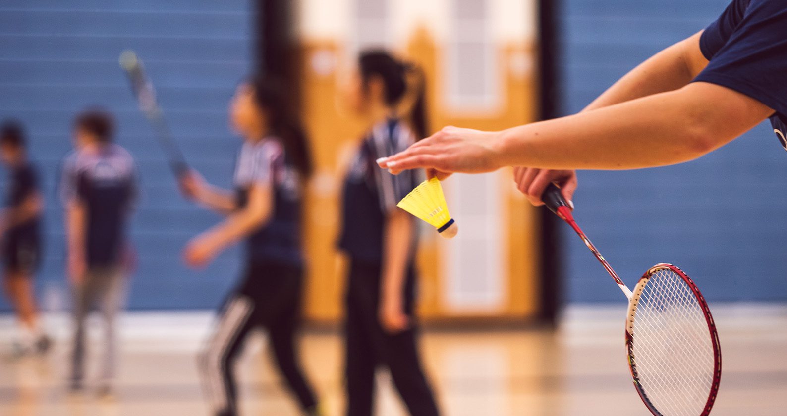 Close-up of a badminton player preparing to serve, holding a racket in one hand and a yellow shuttlecock in the other.