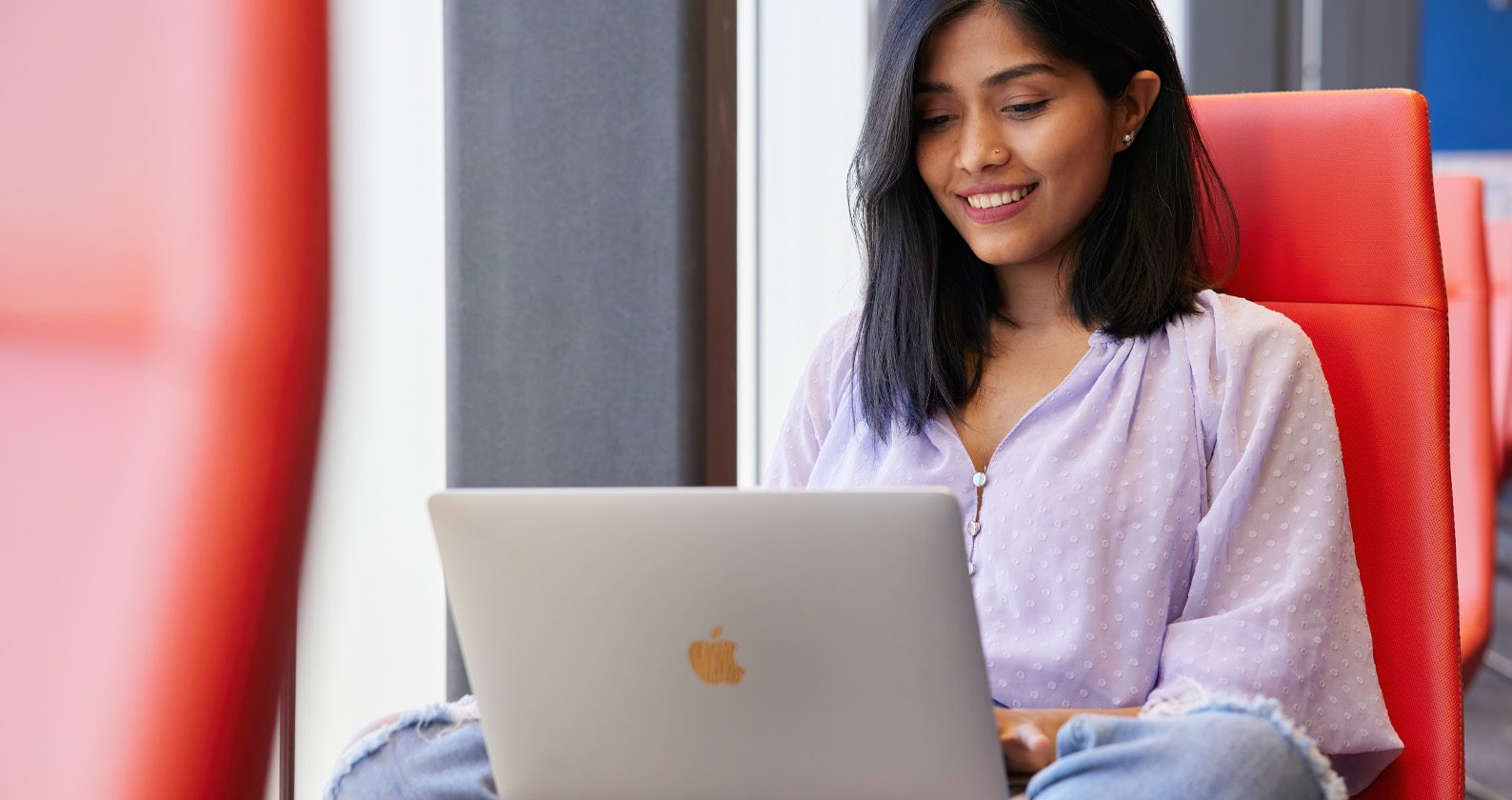Person using a silver laptop on a red chair near a window.