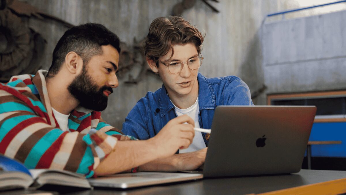 Two people working together at a table, looking at a laptop.