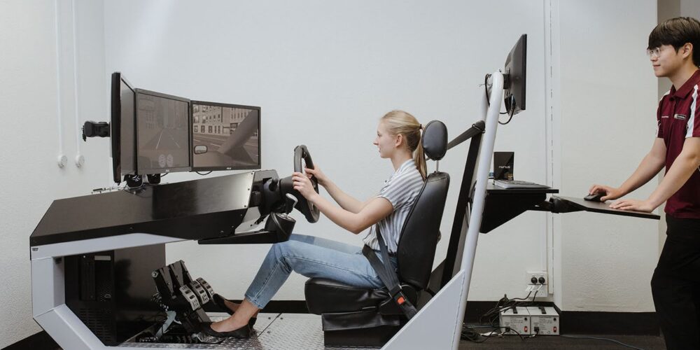 Curtin OT student supervises a young woman driving a simulated car. 
