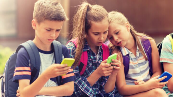 Four young people sitting outdoors, each focused on their own smartphone.