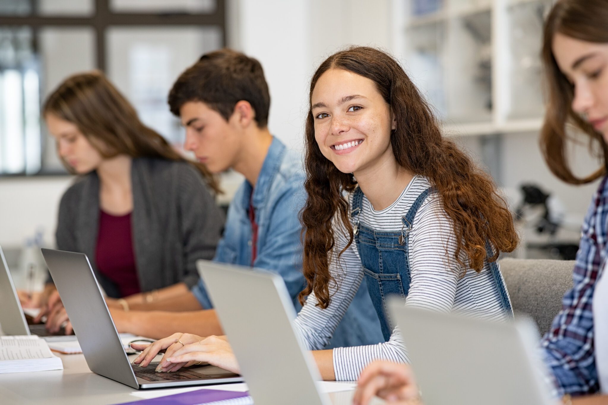 Portrait of smiling university student sitting in a row with classmates, who are all studying together on laptops.