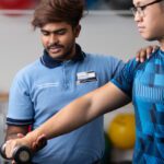 Physiotherapy student guiding a client through an arm strength exercise with a dumbbell in a clinic setting.