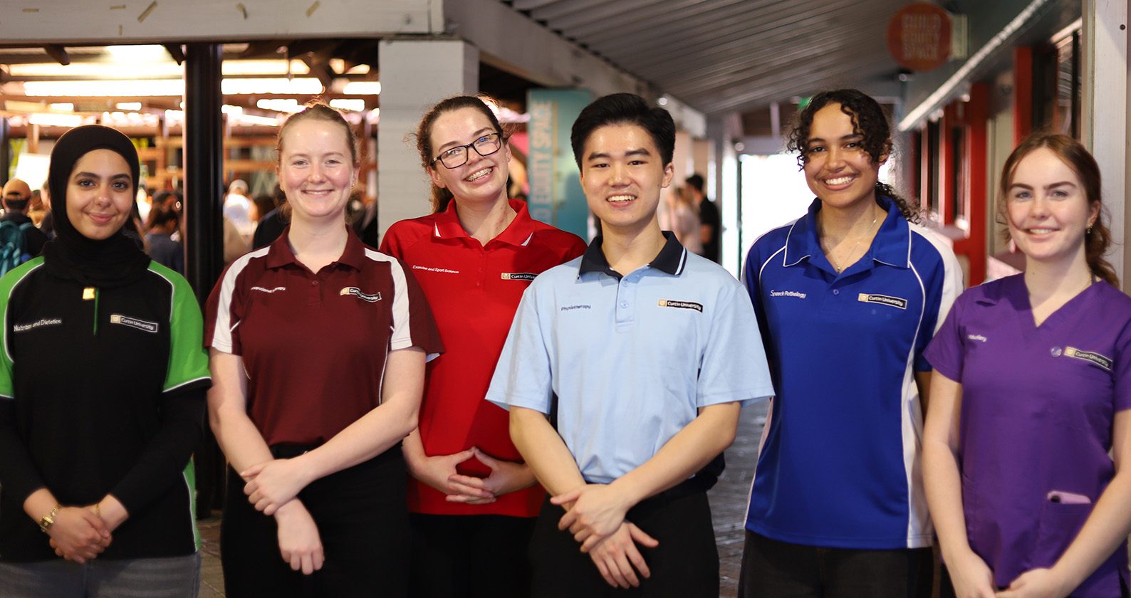 Group of students in different coloured Curtin uniforms standing together in a campus walkway.