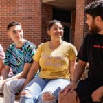 Four students sitting on a wall smiling at each other.