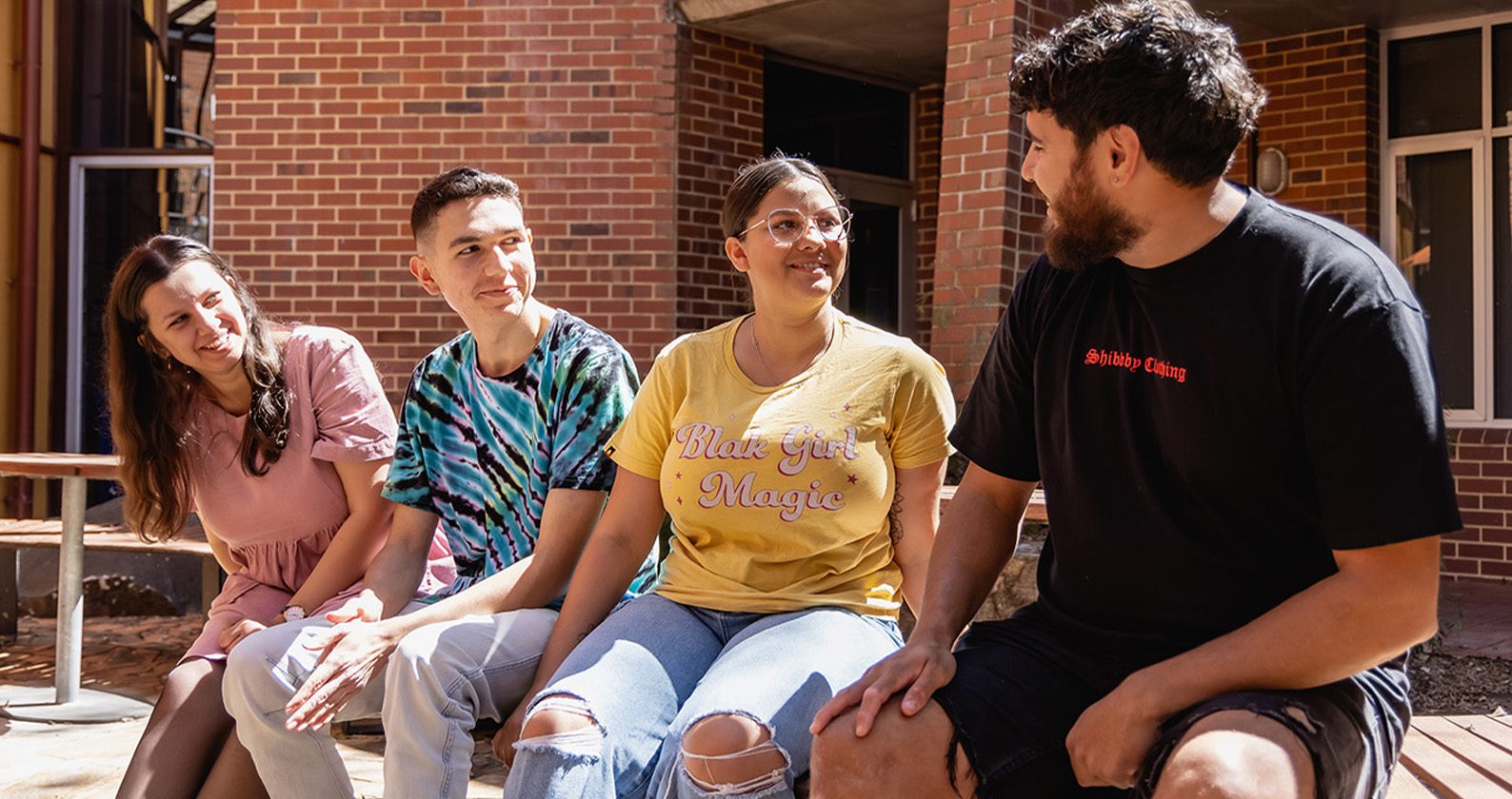 Four students sitting on a wall smiling at each other.