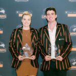 Two people wearing Curtin Carnabys blazers holding sports awards in front of a Curtin University Sport and Recreation backdrop.