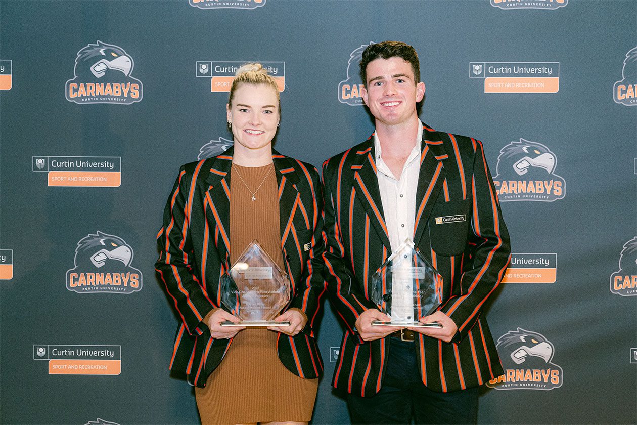 Two people wearing Curtin Carnabys blazers holding sports awards in front of a Curtin University Sport and Recreation backdrop.