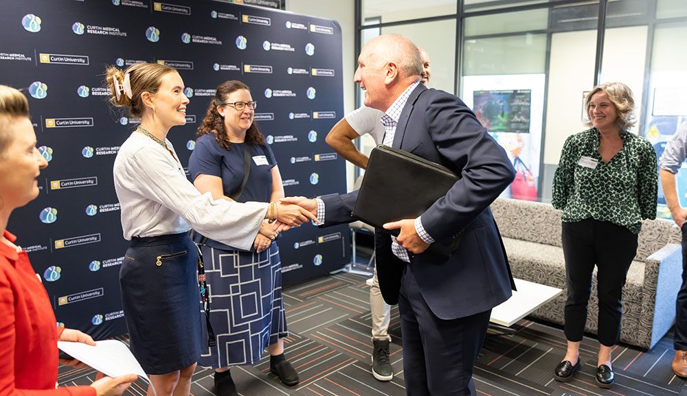 Woman smiling on the left shaking hands with a man in suit.