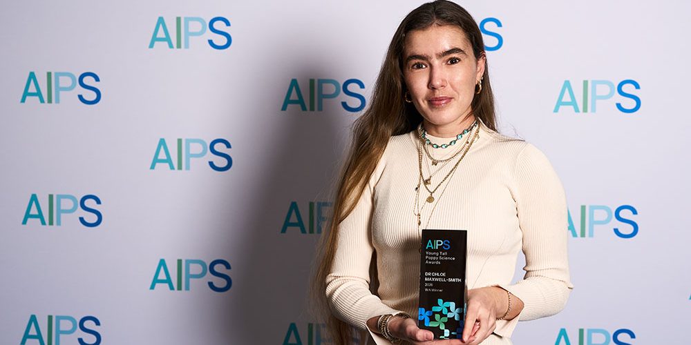 Woman with long brown hair and white top holding tall poppy award