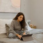 A young woman sitting in bed and has an iPad in her hands