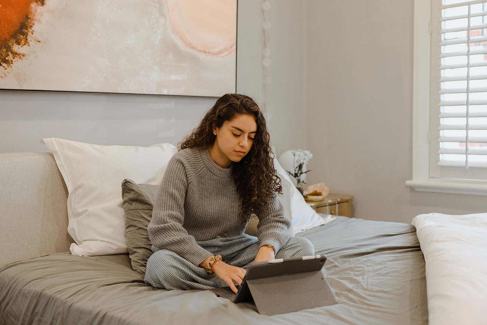 A young woman sitting in bed and has an iPad in her hands