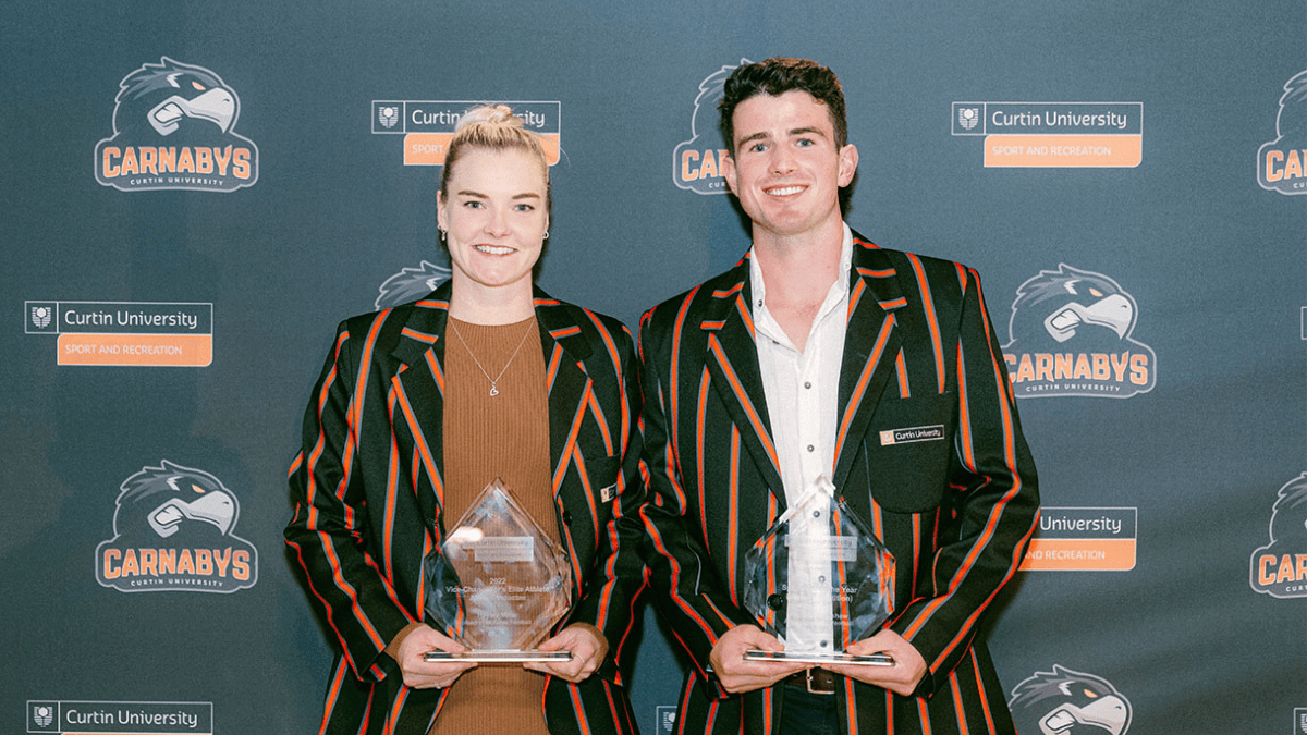 Two people wearing Curtin Carnabys blazers holding sports awards in front of a Curtin University Sport and Recreation backdrop.