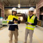 Student Nathan Moore on the right on a construction site speaking with a supervisor on the left.