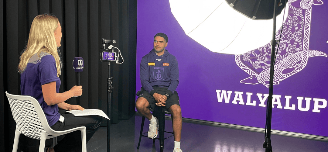 Two people taking part in a filmed interview in a Fremantle Dockers media studio.