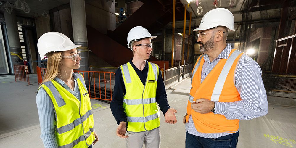 A man and two students in high vis and hard hats on a construction site.