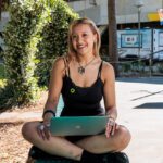 Student sitting outdoors holding a laptop.