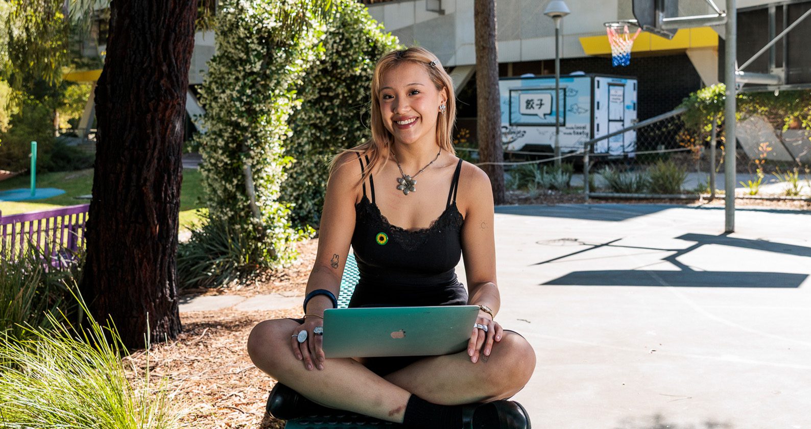 Student sitting outdoors holding a laptop.