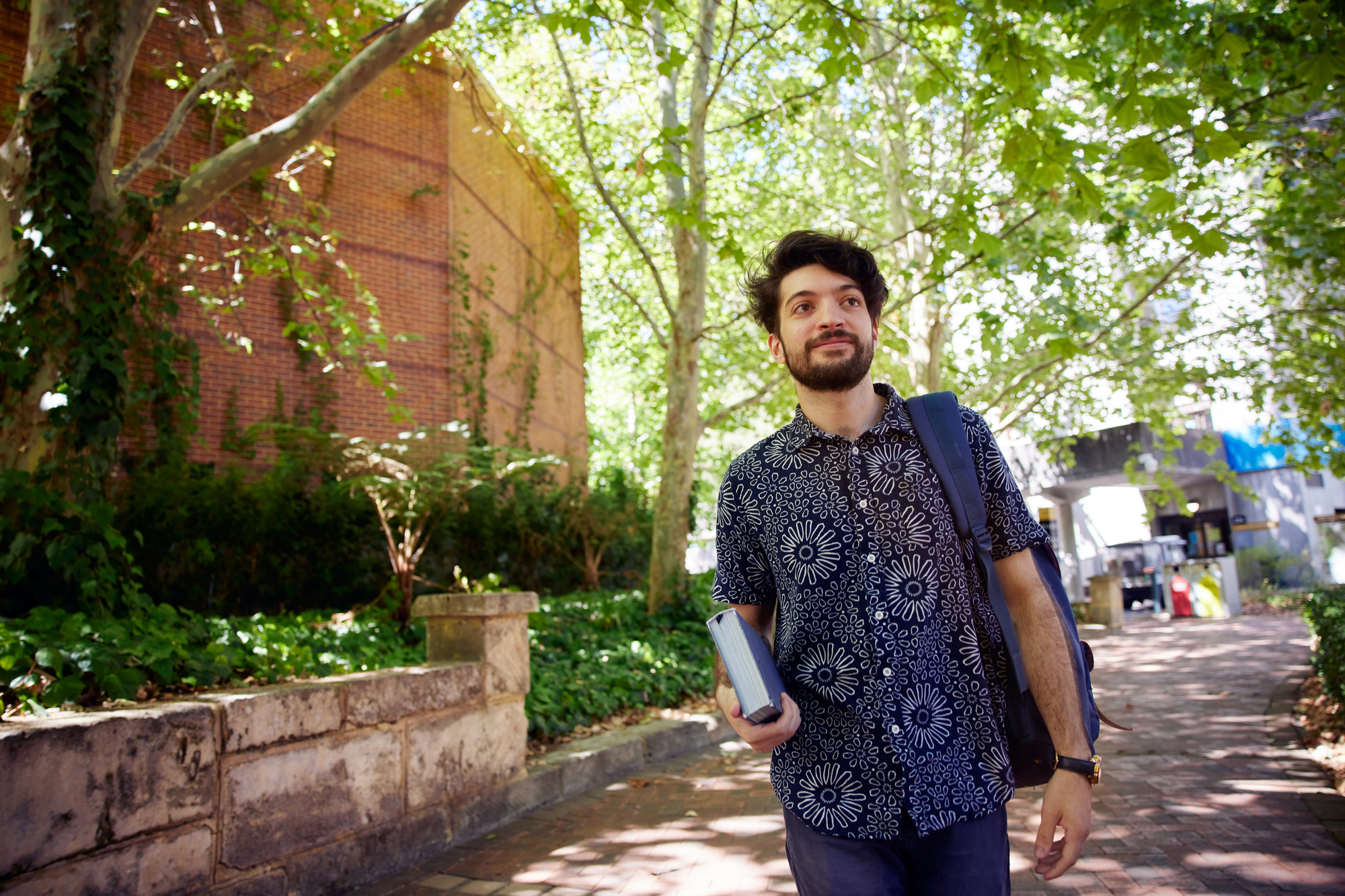 Male student walking through leafy campus